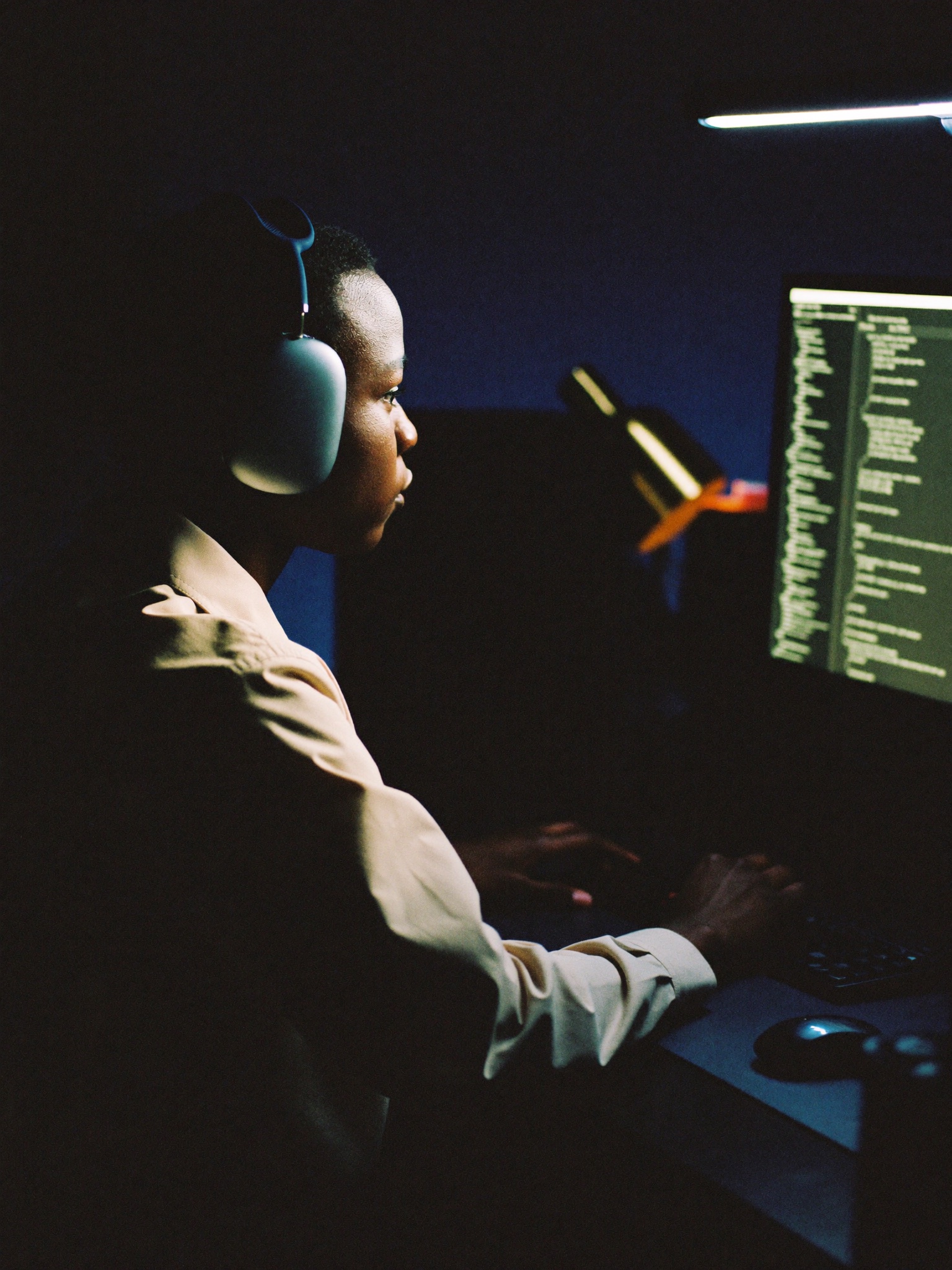 Developer in headphones coding at night by warm lamplight